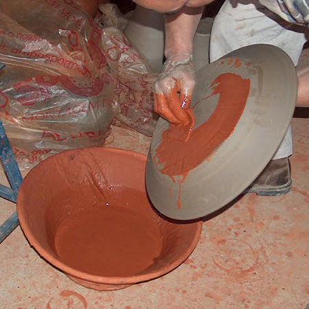 Processo de tingimento da peça com barro vermelho, utilizando a aplanata